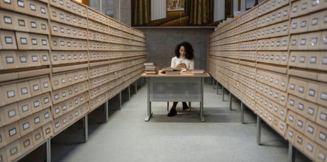 a girl sitting in front of a table between database wooden drawer